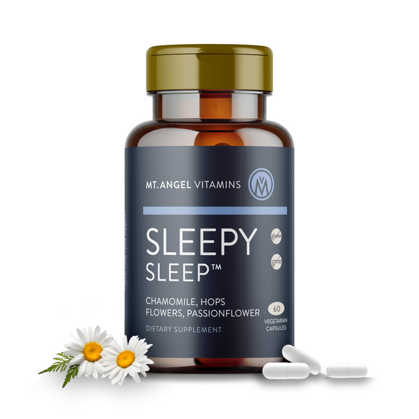 Picture of blue bottle of Mt. Angel Vitamins Sleepy Sleepy Dietary Supplement on a white background, surrounded by white capsules and chamomile flowers